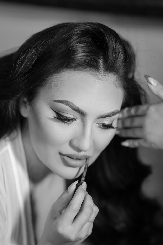 Bride applying lipstick during wedding preparation in black and white