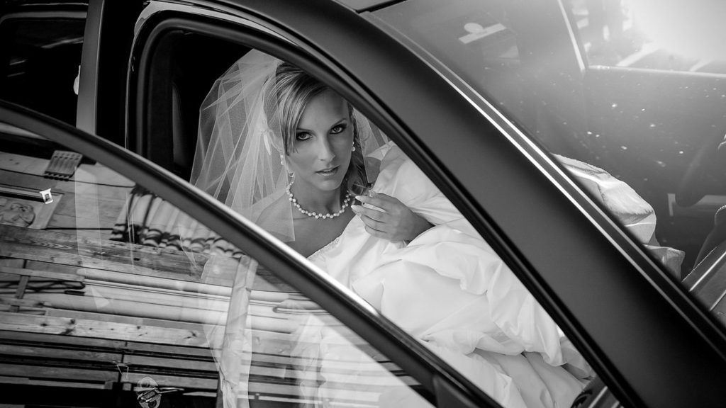 Bride sitting in car looking out window in black and white