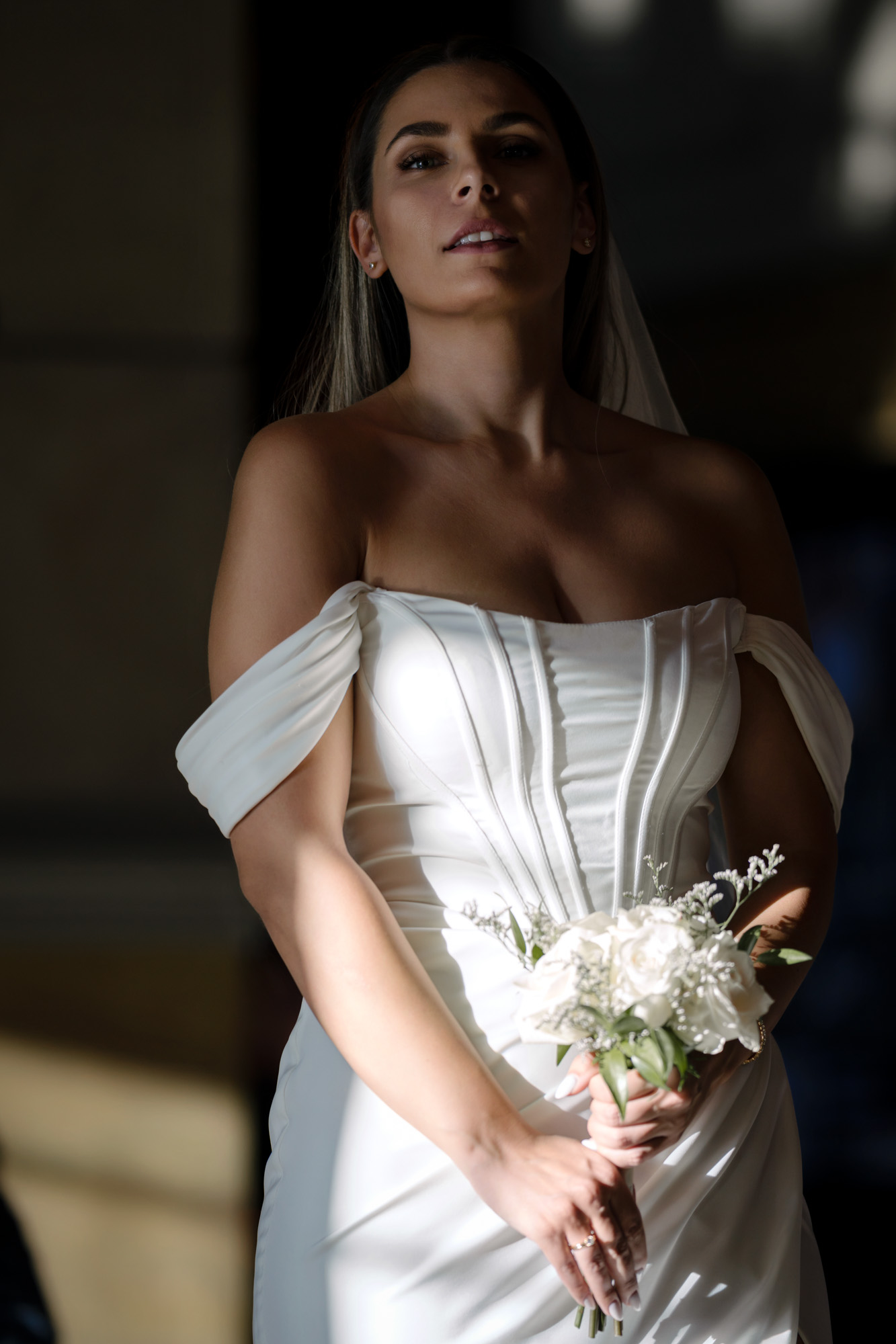 Elegant bridal portrait with dramatic light and shadow of bride holding bouquet