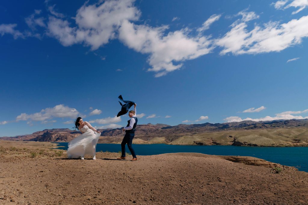 Playful couple dancing in wind above Colorado River desert landscape near Las Vegas Nevada elopement