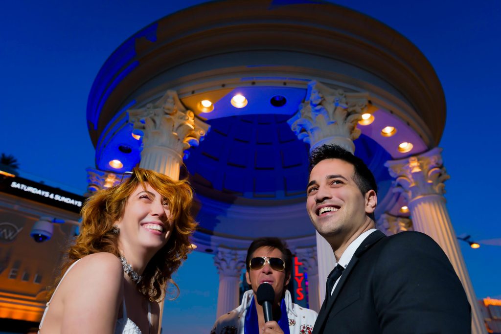 Las Vegas Elvis elopement couple portrait at Caesars Palace gazebo at night with Elvis officiant in background, photographed by Zoltan Redl-Nagy