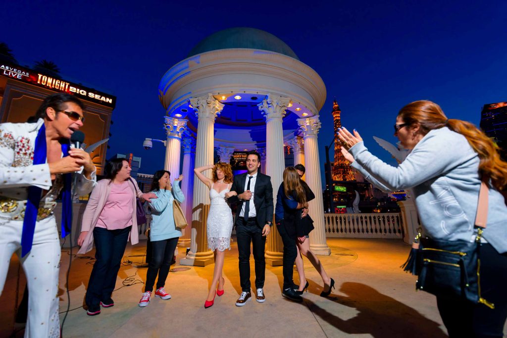 Las Vegas Elvis elopement celebration with couple and guests clapping at Caesars Palace gazebo at night with Eiffel Tower in background, photographed by Zoltan Redl-Nagy