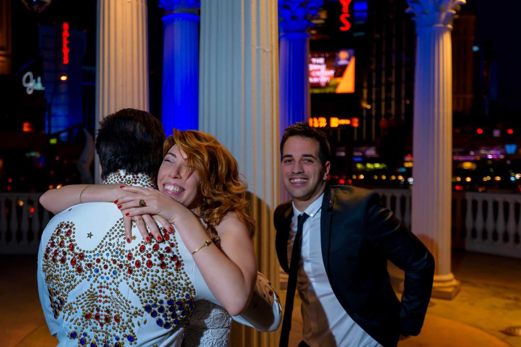 Las Vegas Elvis elopement candid moment with bride hugging Elvis officiant at Caesars Palace gazebo at night, photographed by Zoltan Redl-Nagy