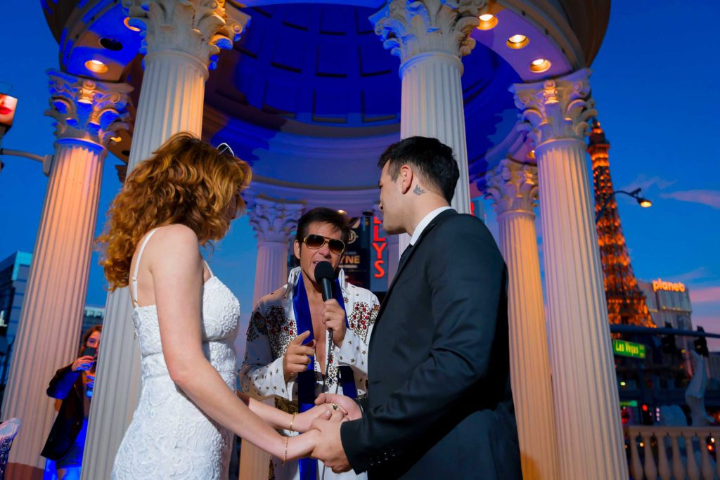 Las Vegas Elvis elopement ceremony with couple holding hands at Caesars Palace gazebo at night with Eiffel Tower in background, photographed by Zoltan Redl-Nagy