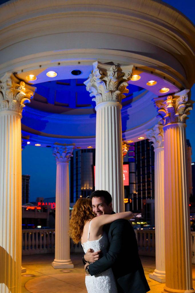 Romantic Las Vegas elopement couple embracing at Caesars Palace gazebo at night with city lights in background, photographed by Zoltan Redl-Nagy