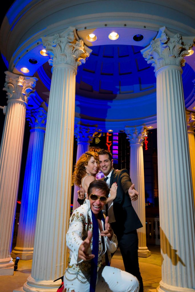 Las Vegas Elvis elopement at Caesars Palace gazebo at night with Elvis officiant in foreground and couple posing behind, fun wedding moment, photographed by Zoltan Redl-Nagy