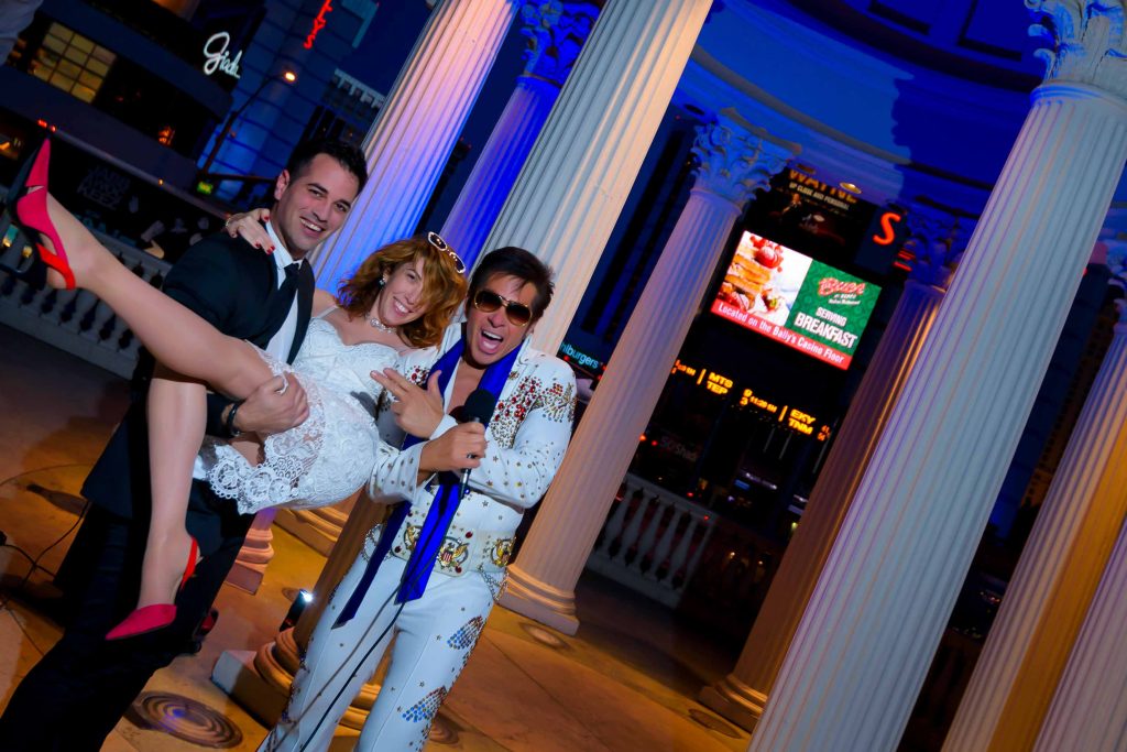 Las Vegas Elvis elopement at Caesars Palace gazebo with groom carrying bride and Elvis officiant celebrating at night, fun wedding moment, photographed by Zoltan Redl-Nagy