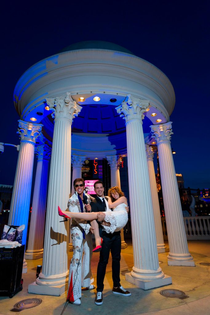Las Vegas Elvis elopement at Caesars Palace gazebo at night with groom holding bride and Elvis officiant celebrating, fun wedding moment, photographed by Zoltan Redl-Nagy