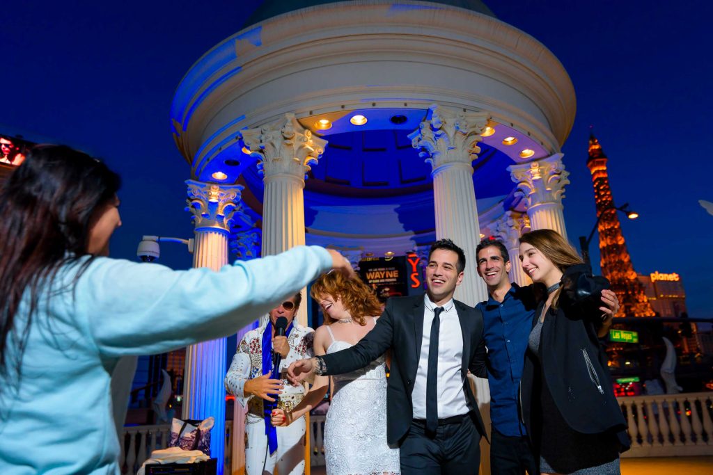 Las Vegas Elvis elopement group celebration at Caesars Palace gazebo at night with Eiffel Tower in background, joyful wedding moment, photographed by Zoltan Redl-Nagy