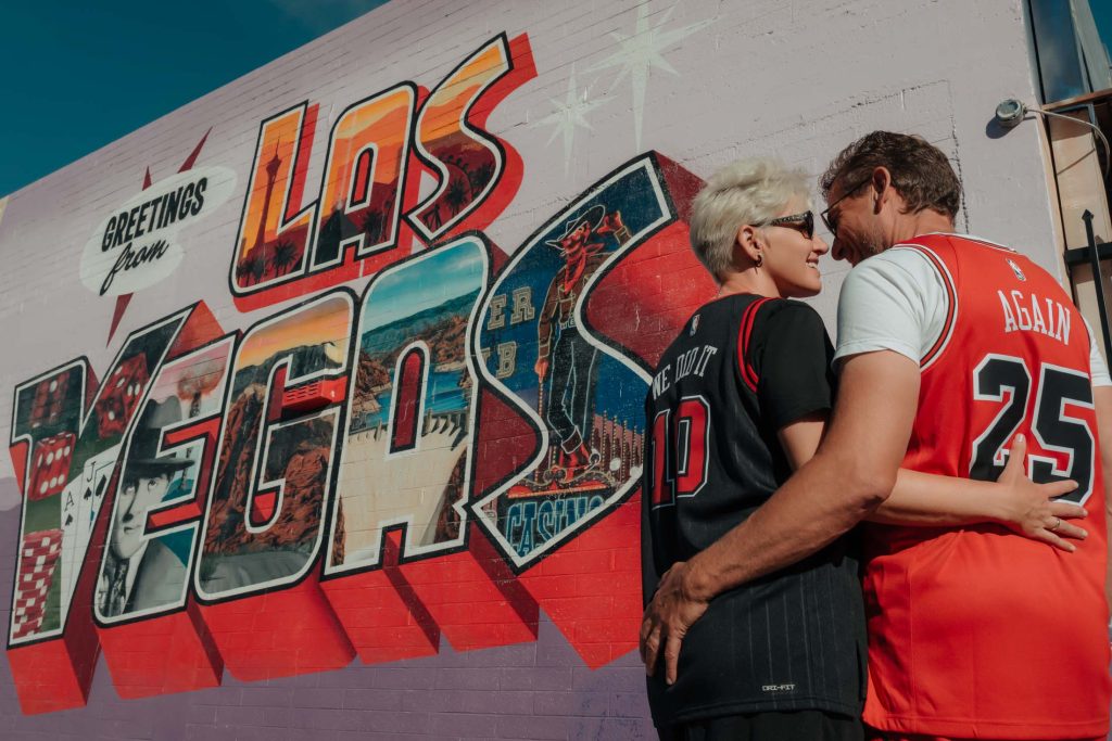 Renewal elopement couple embracing in front of Greetings from Las Vegas mural in Arts District, photographed by Zoltan Redl Nagy.