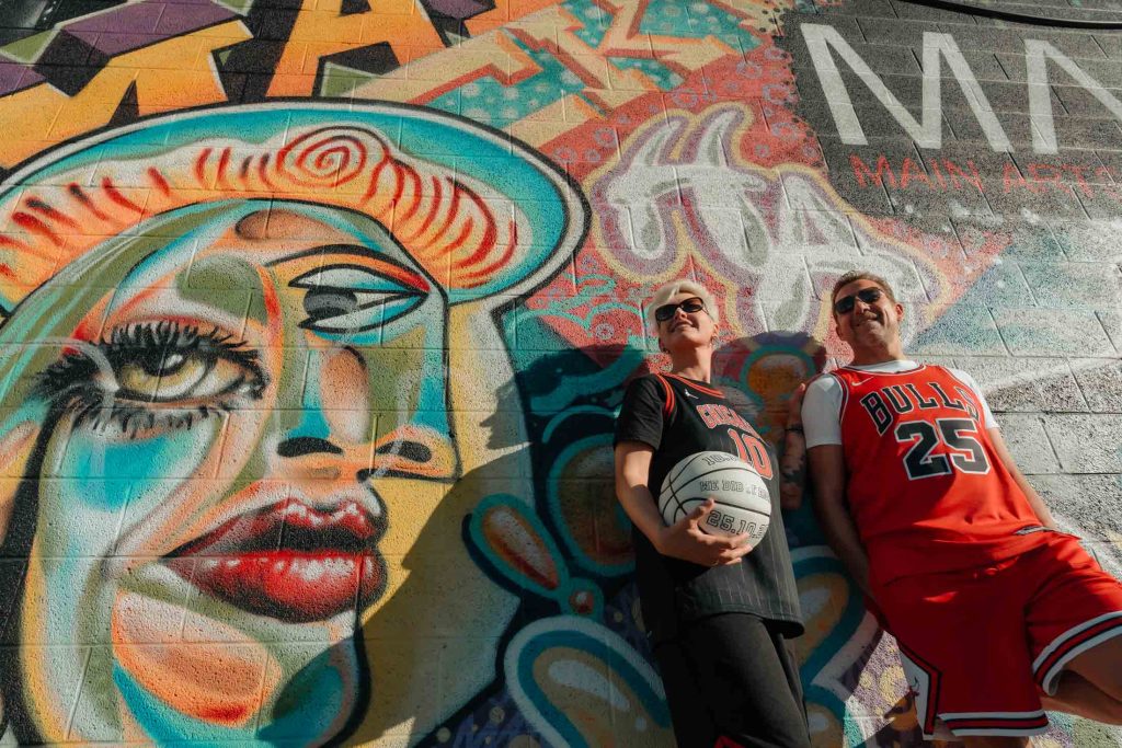Renewal elopement couple in Las Vegas Arts District leaning against colorful mural with basketball, photographed by Zoltan Redl Nagy.