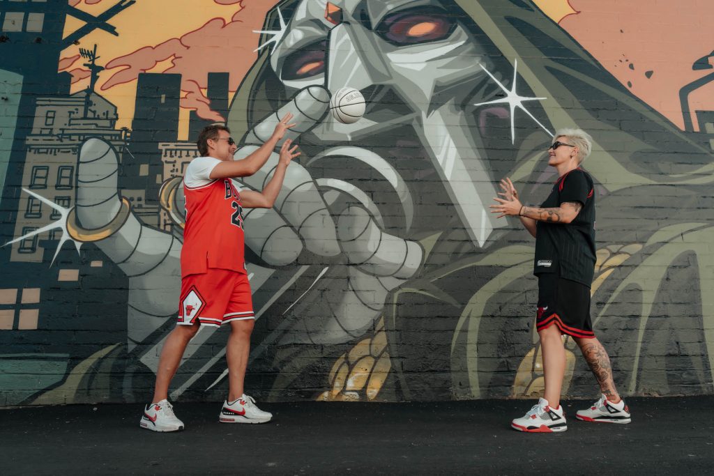 Renewal elopement couple in Las Vegas Arts District tossing a baseball in front of a colorful urban mural, photographed by Zoltan Redl Nagy.