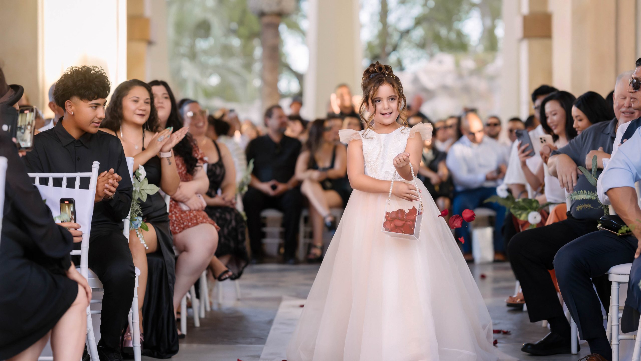 Flower girl walking down the aisle during a Mandalay Bay Las Vegas wedding ceremony surrounded by smiling guests