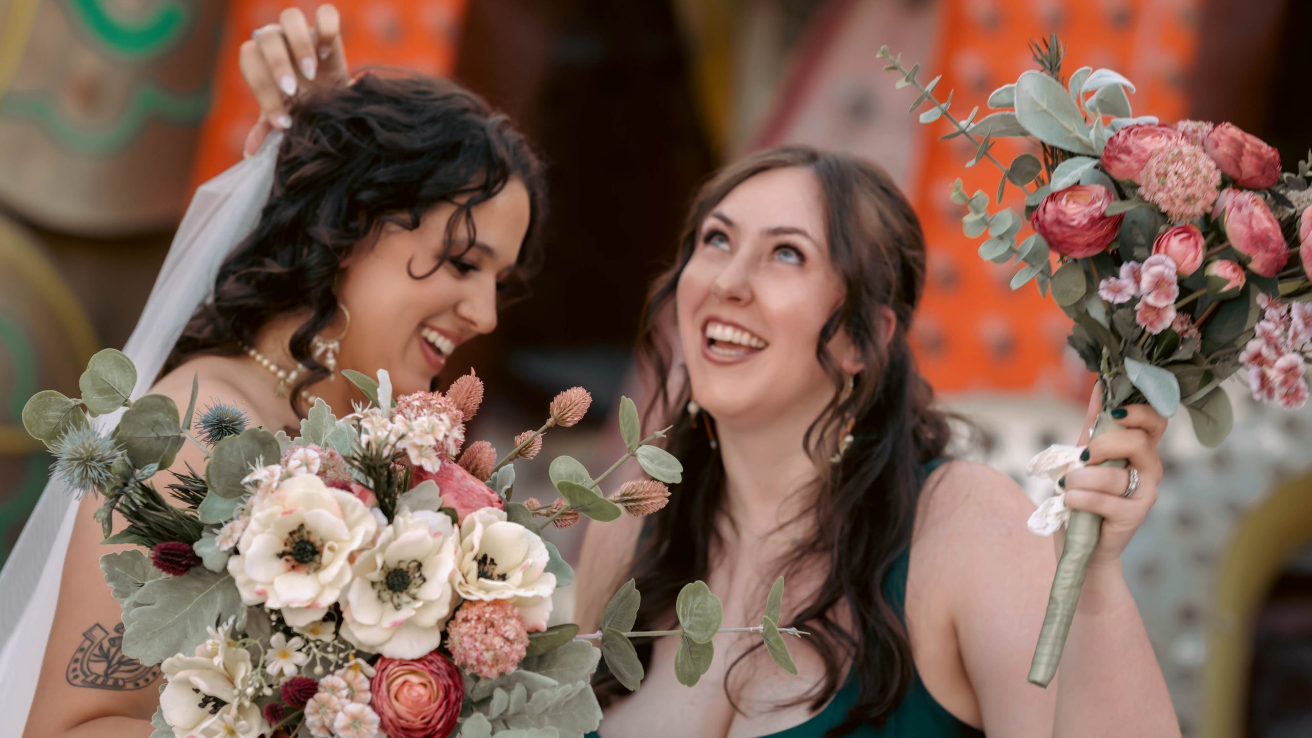 Emotional bridesmaid moment at the Neon Museum Las Vegas with bride holding colorful wedding bouquets and sharing joyful laughter