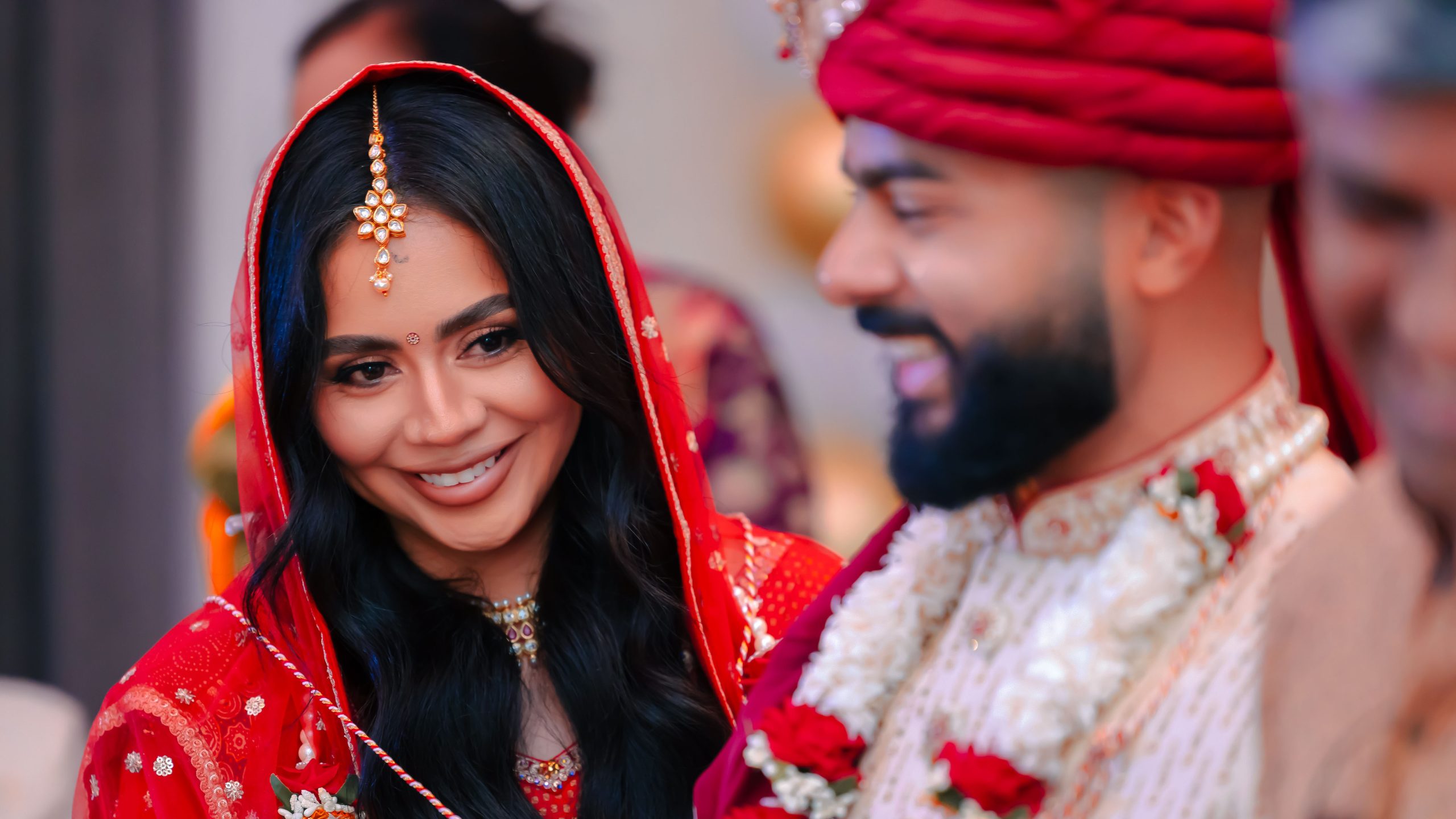 Smiling Indian bride in traditional red wedding attire during a Hindu wedding ceremony beside the groom.