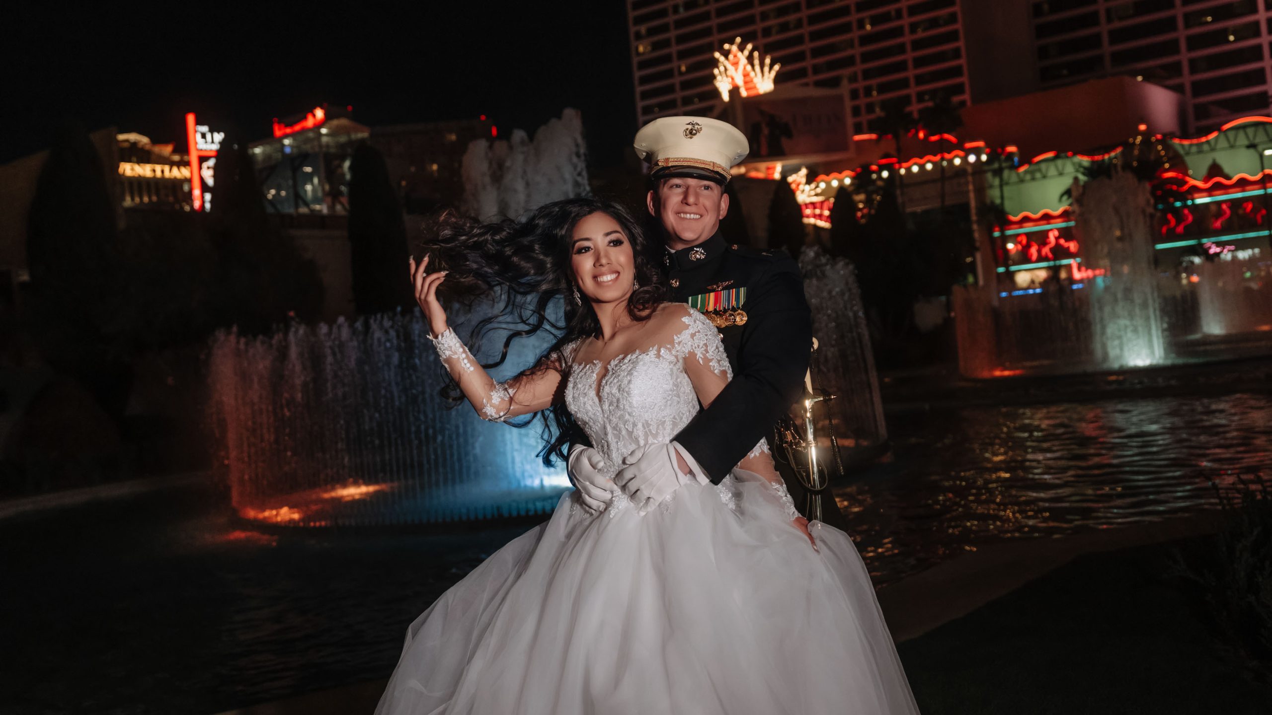 Romantic Caesars Palace wedding portrait at night featuring a U.S. Marine groom and bride by the illuminated fountains on the Las Vegas Strip.
