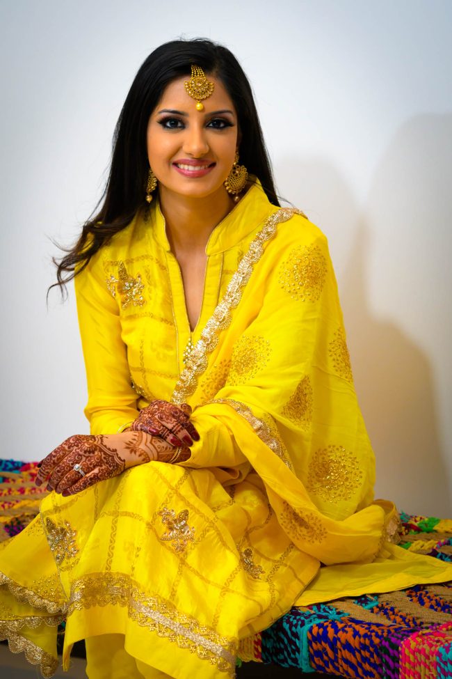 indian bride portrait in yellow mehndi ceremony outfit with henna hands