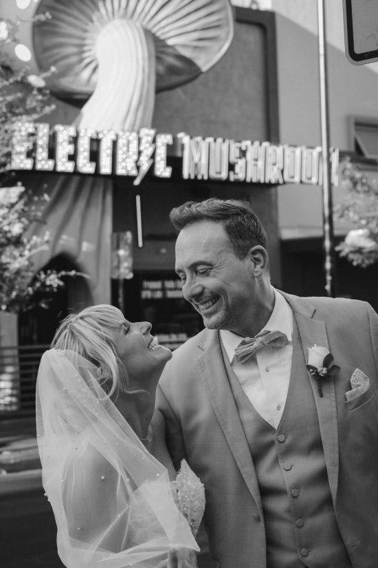 Romantic Las Vegas Downtown elopement couple smiling together in front of the iconic Electric Mushroom on Fremont East in a timeless black and white wedding portrait.