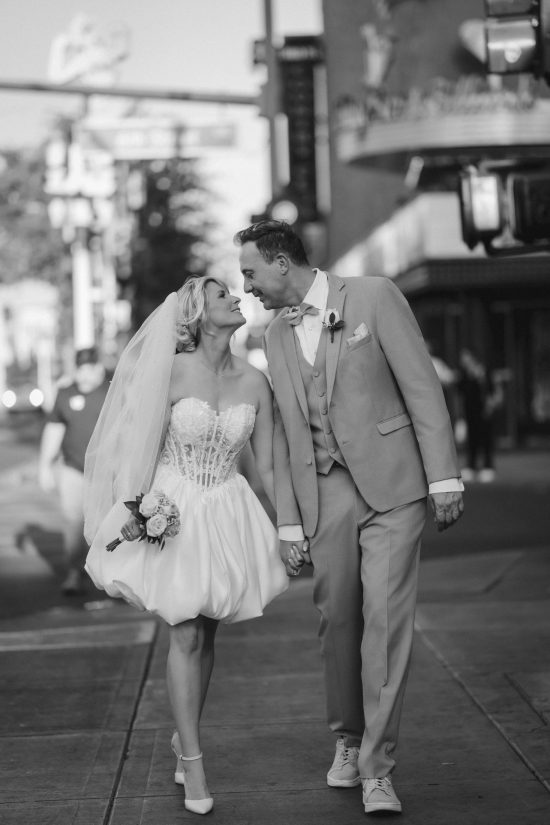Romantic Las Vegas Downtown elopement couple walking hand in hand through Fremont Street in a timeless black and white wedding portrait.