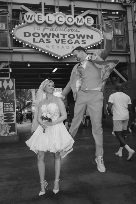 Las Vegas Downtown elopement couple celebrating beneath the Welcome to Fabulous Downtown Las Vegas sign in a timeless black and white wedding portrait.