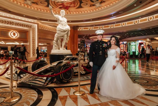 Bride and U.S. Marine groom posing beside a Formula 1 race car inside Caesars Palace during the Las Vegas Grand Prix weekend.