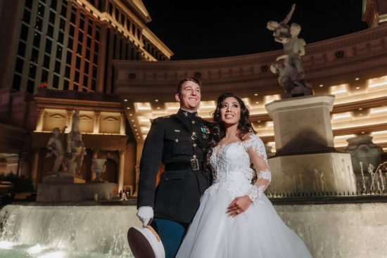 Luxury Caesars Palace wedding portrait at night with a U.S. Marine groom and bride standing beside the illuminated Fountain of the Gods in Las Vegas.