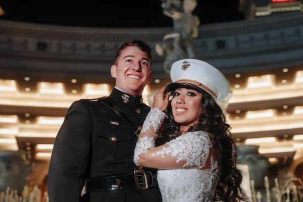 Bride wearing a U.S. Marine dress cap beside her groom during a nighttime Caesars Palace wedding portrait in Las Vegas.
