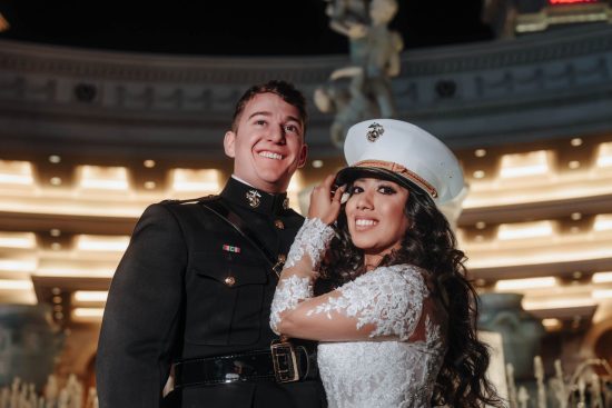 Bride wearing a U.S. Marine dress cap beside her groom during a nighttime Caesars Palace wedding portrait in Las Vegas.