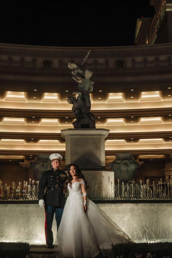 Luxury Caesars Palace wedding portrait at night featuring a U.S. Marine groom and bride beside the Fountain of the Gods in Las Vegas.