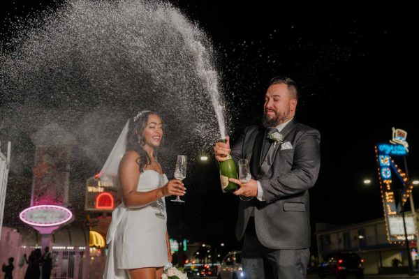 Bride and groom celebrating with a champagne spray outside Little White Chapel at night in Las Vegas