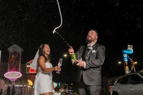 Bride and groom celebrating with a champagne spray outside Little White Chapel at night in Las Vegas